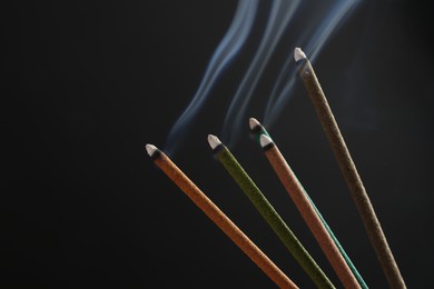 Photo of Aromatic incense sticks smoldering on black background