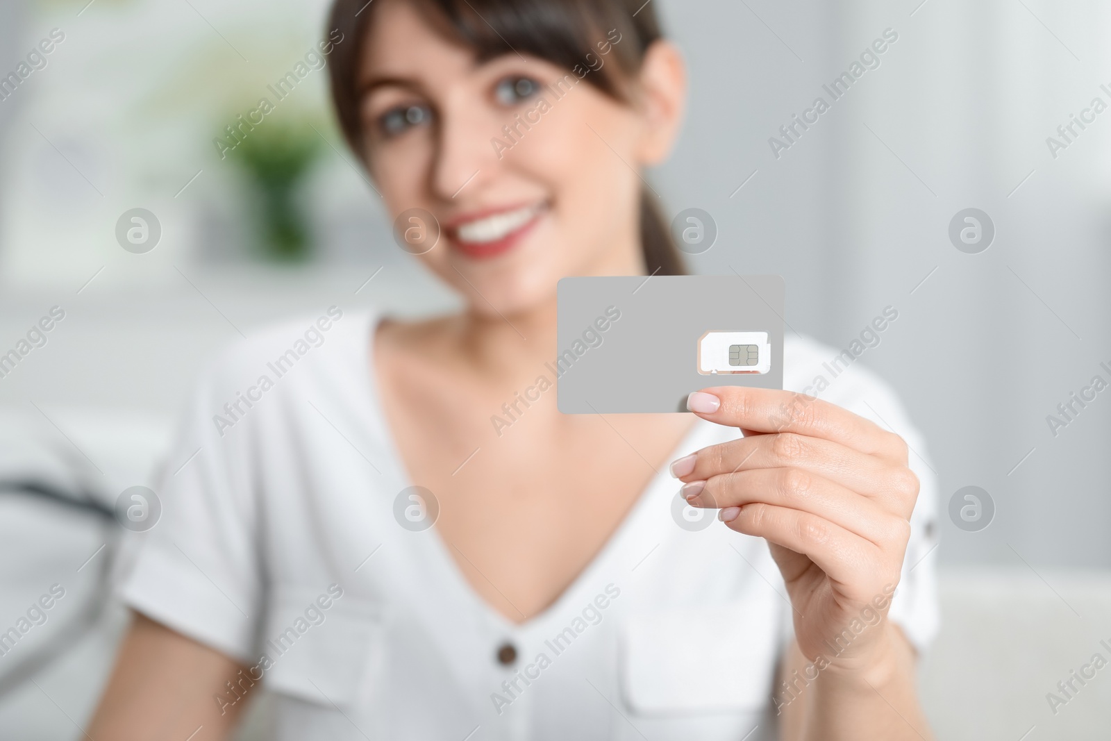 Photo of Woman holding SIM card indoors, selective focus