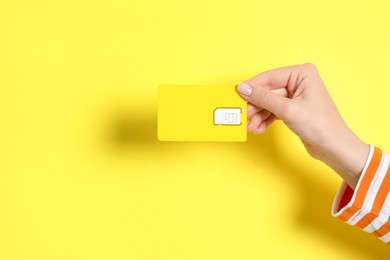 Photo of Woman holding SIM card on yellow background, closeup