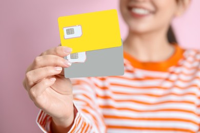 Photo of Woman holding SIM cards on pink background, closeup