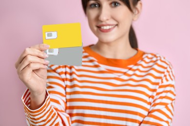 Photo of Woman holding SIM cards on pink background, selective focus