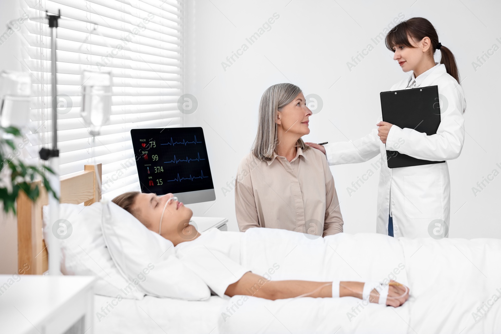 Photo of Coma patient. Sad mature woman near her unconscious son talking with doctor in hospital