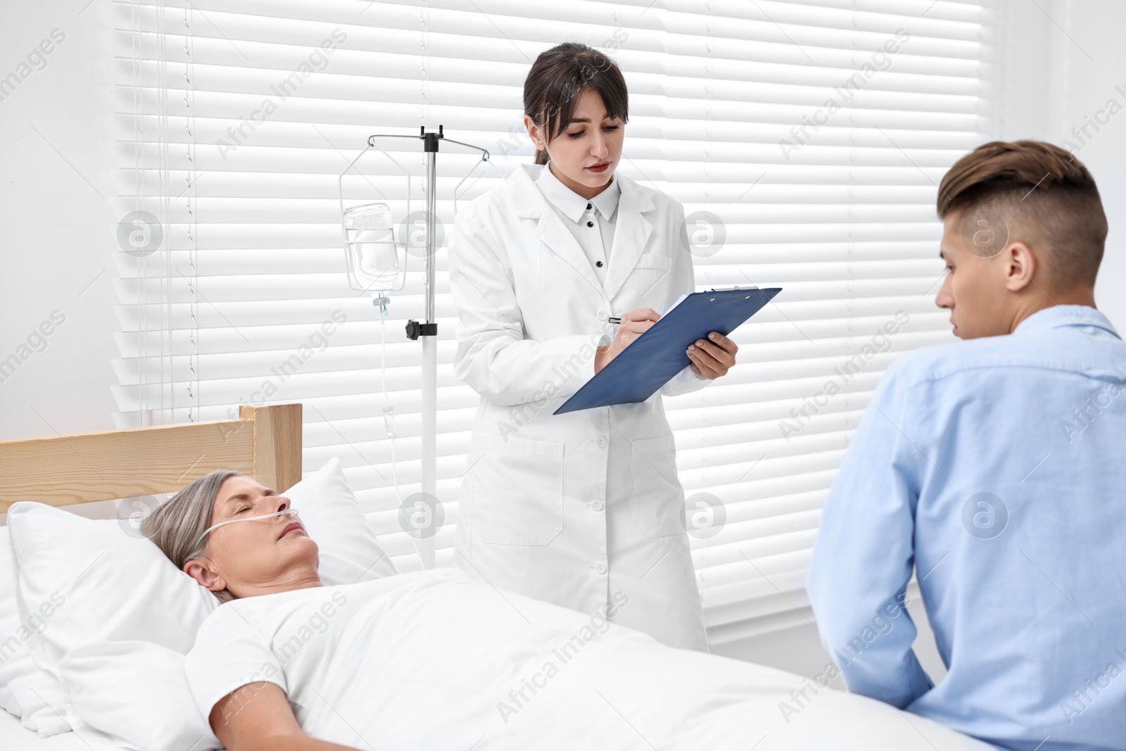 Photo of Coma patient. Sad young man near his unconscious mother talking with doctor in hospital