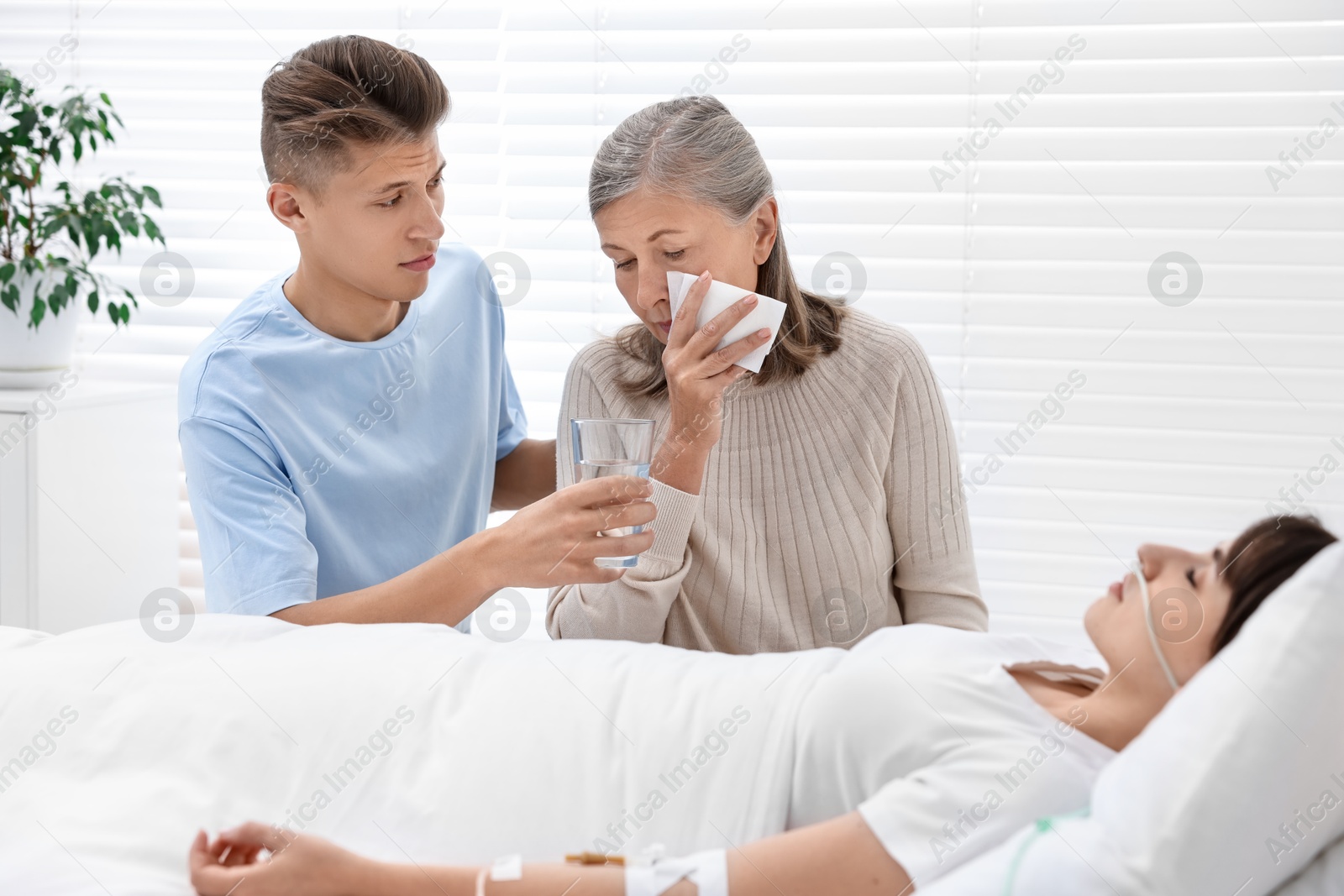 Photo of Coma patient. Sad relatives near sleeping young woman in hospital