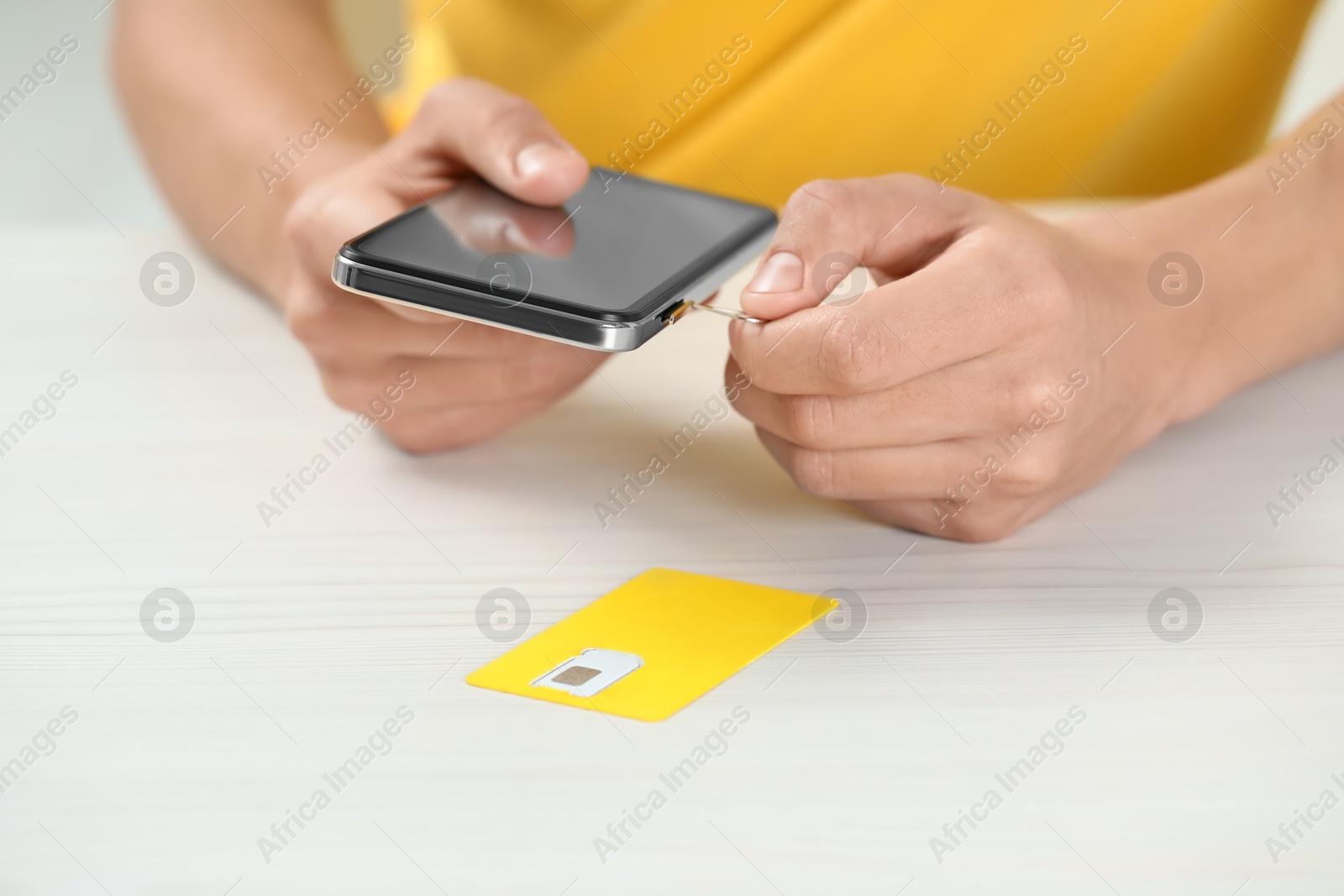 Photo of Man with ejector opening SIM card tray in smartphone at white wooden table, closeup