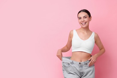 Photo of Diet and weight loss concept. Happy young woman in big jeans showing her slim body on pink background. Space for text