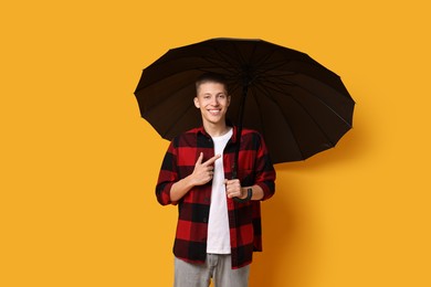 Photo of Young man with black umbrella on yellow background