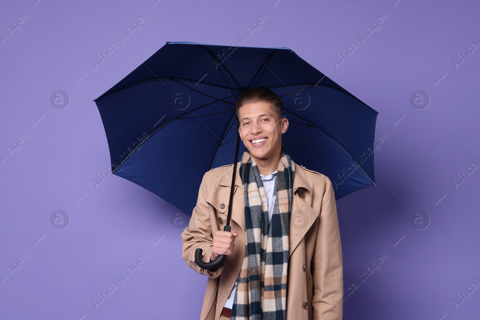 Photo of Young man with blue umbrella on purple background