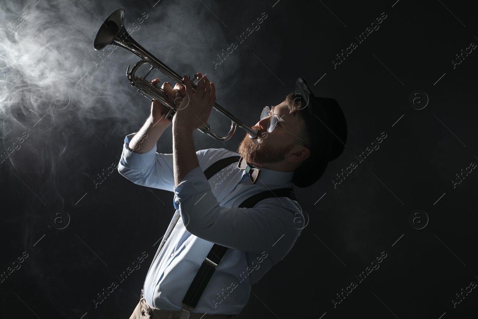 Photo of Professional musician playing trumpet on black background with smoke