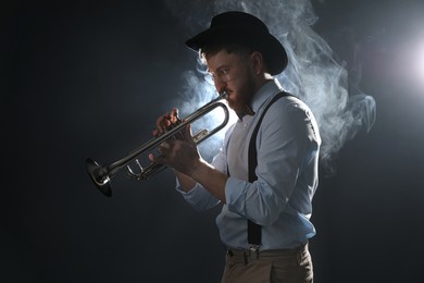 Professional musician playing trumpet on dark background with smoke