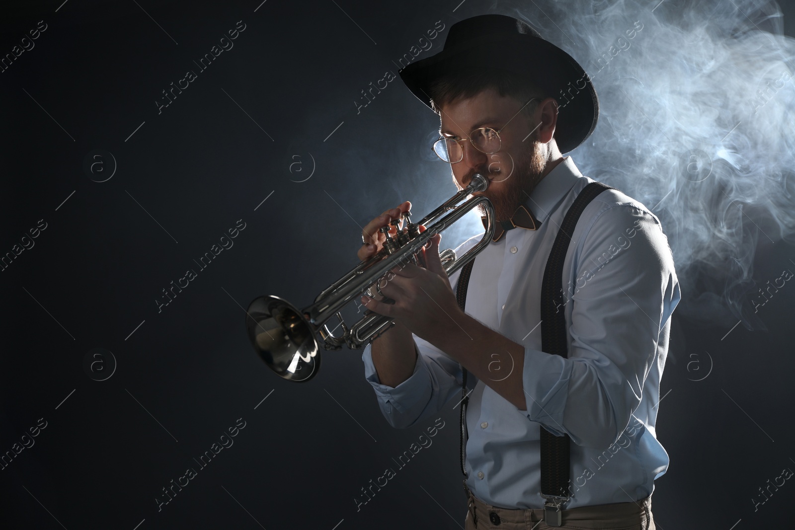 Photo of Professional musician playing trumpet on dark background with smoke. Space for text