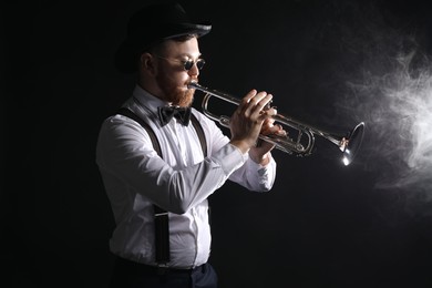 Photo of Professional musician playing trumpet on black background with smoke