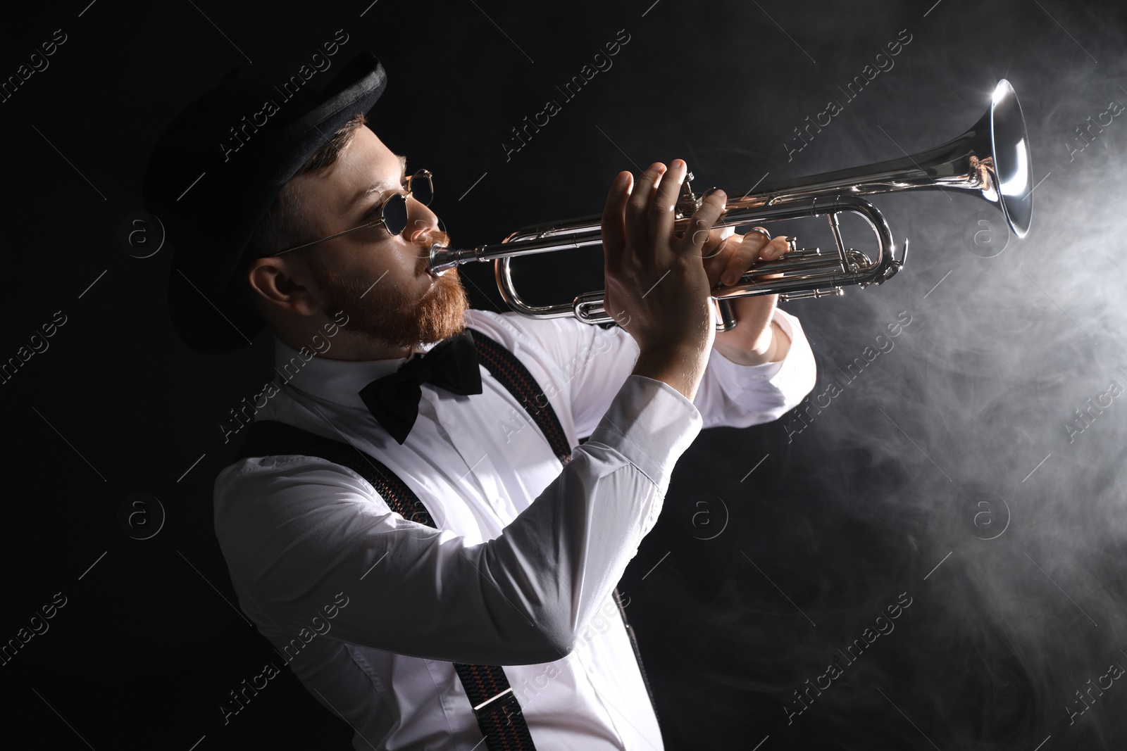 Photo of Professional musician playing trumpet on black background with smoke