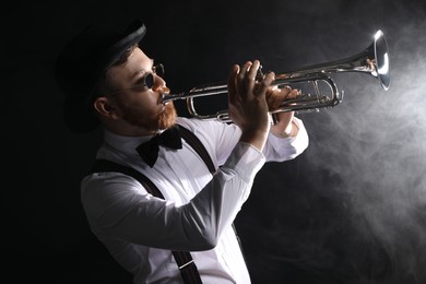 Professional musician playing trumpet on black background with smoke