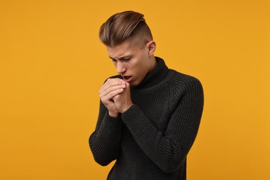 Photo of Sick man coughing on orange background. Cold symptoms