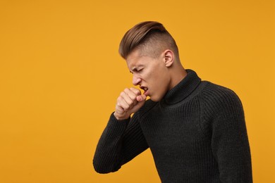 Photo of Sick man coughing on orange background, space for text. Cold symptoms