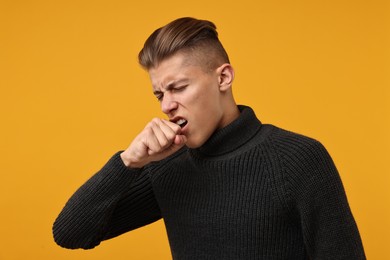 Photo of Sick man coughing on orange background. Cold symptoms