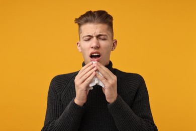 Photo of Sick man with tissue sneezing on orange background. Cold symptoms