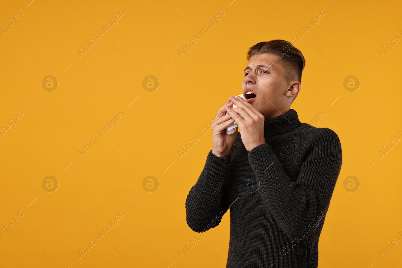 Photo of Cold symptoms. Sick man with tissue sneezing on orange background, space for text