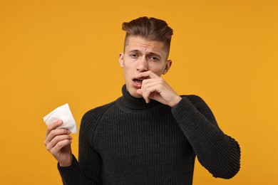 Photo of Sick man with tissue suffering from cold symptoms on orange background