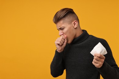 Photo of Cold symptoms. Sick man with tissue coughing on orange background, space for text