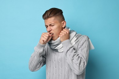Photo of Sick man coughing on light blue background. Cold symptoms
