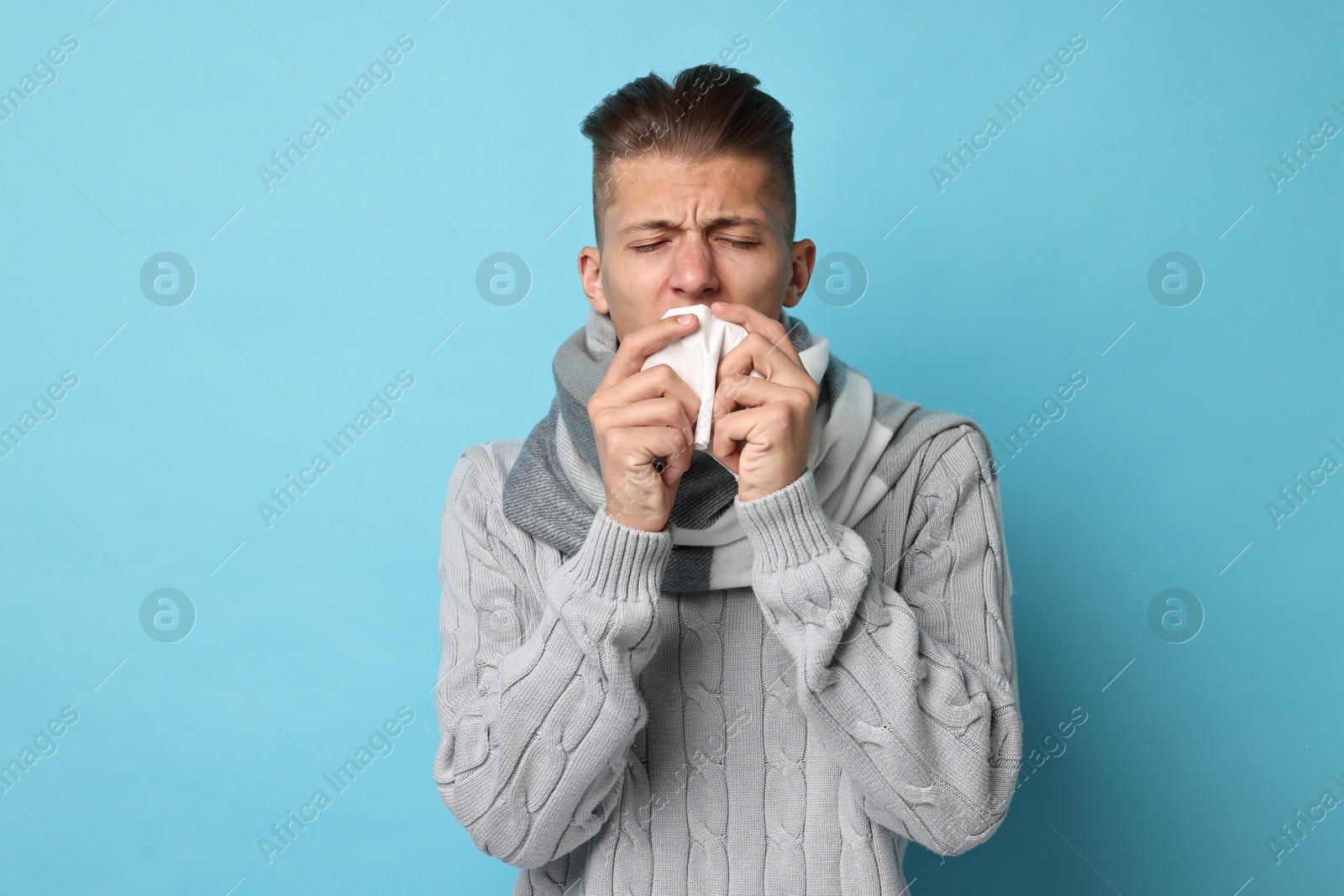 Photo of Sick man with tissue suffering from cold symptoms on light blue background