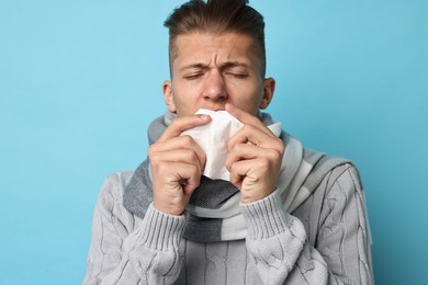 Photo of Sick man with tissue suffering from cold symptoms on light blue background
