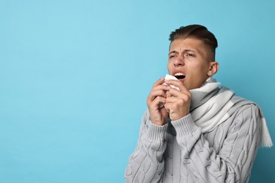Photo of Cold symptoms. Sick man with tissue sneezing on light blue background, space for text