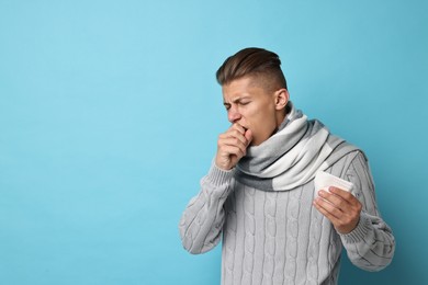 Photo of Sick man with tissue suffering from cold symptoms on light blue background, space for text