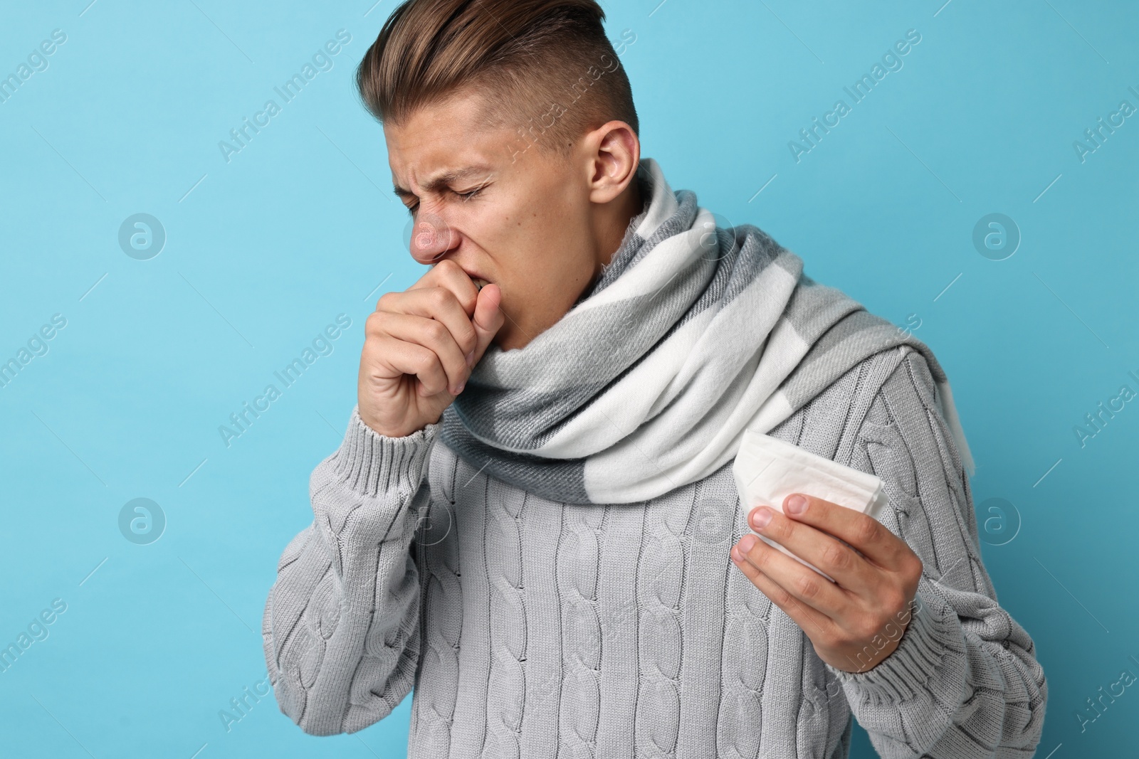 Photo of Sick man with tissue suffering from cold symptoms on light blue background