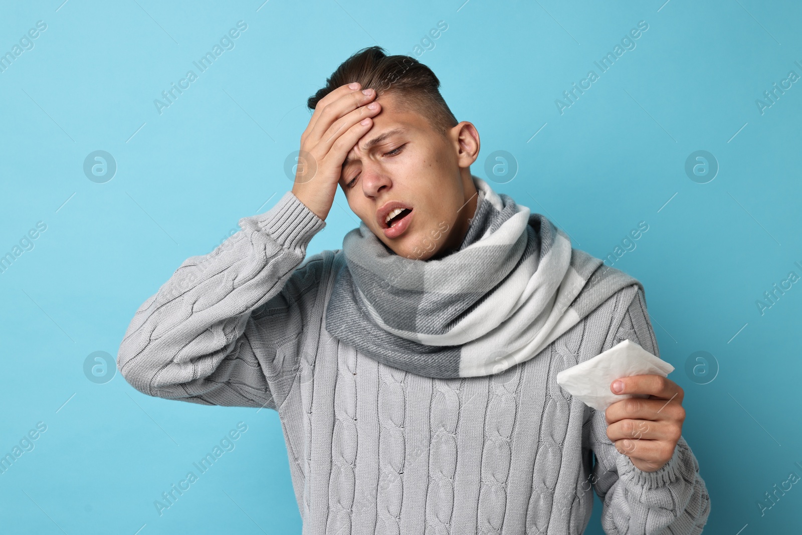 Photo of Sick man with tissue suffering from cold symptoms on light blue background