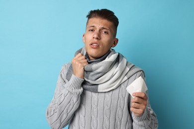 Photo of Sick man with tissue suffering from cold symptoms on light blue background