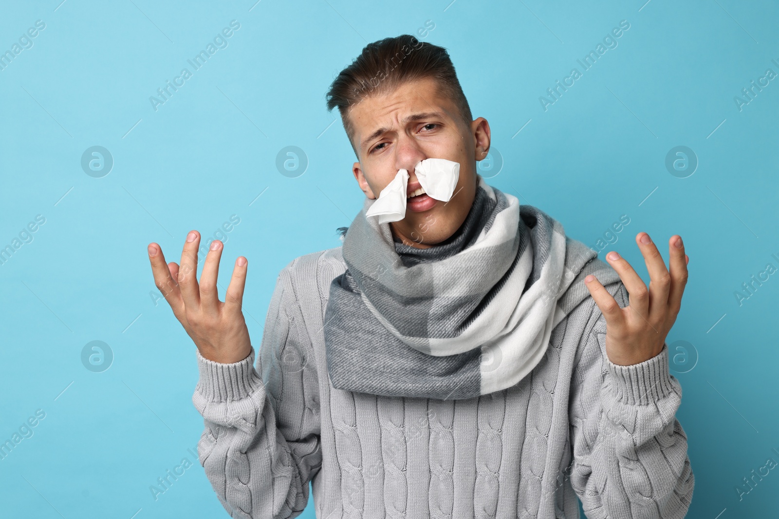 Photo of Sick man with tissue suffering from cold symptoms on light blue background