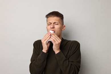 Photo of Sick man with tissue suffering from cold symptoms on light grey background