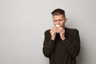 Photo of Sick man with tissue suffering from cold symptoms on light grey background, space for text