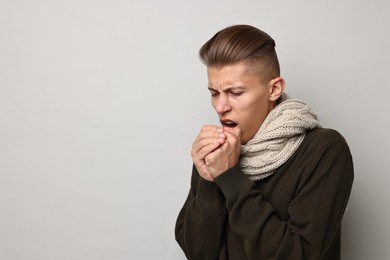 Photo of Cold symptoms. Sick man coughing on light grey background, space for text