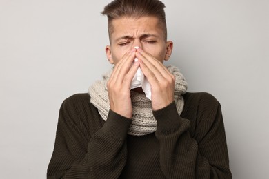 Photo of Sick man with tissue blowing runny nose on light grey background. Cold symptoms