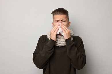 Photo of Sick man with tissue blowing runny nose on light grey background. Cold symptoms