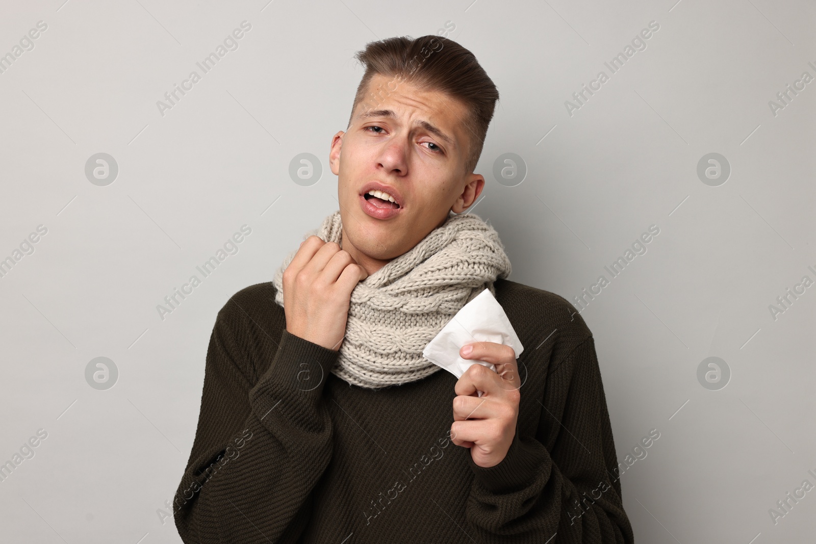 Photo of Sick man with tissue suffering from cold symptoms on light grey background