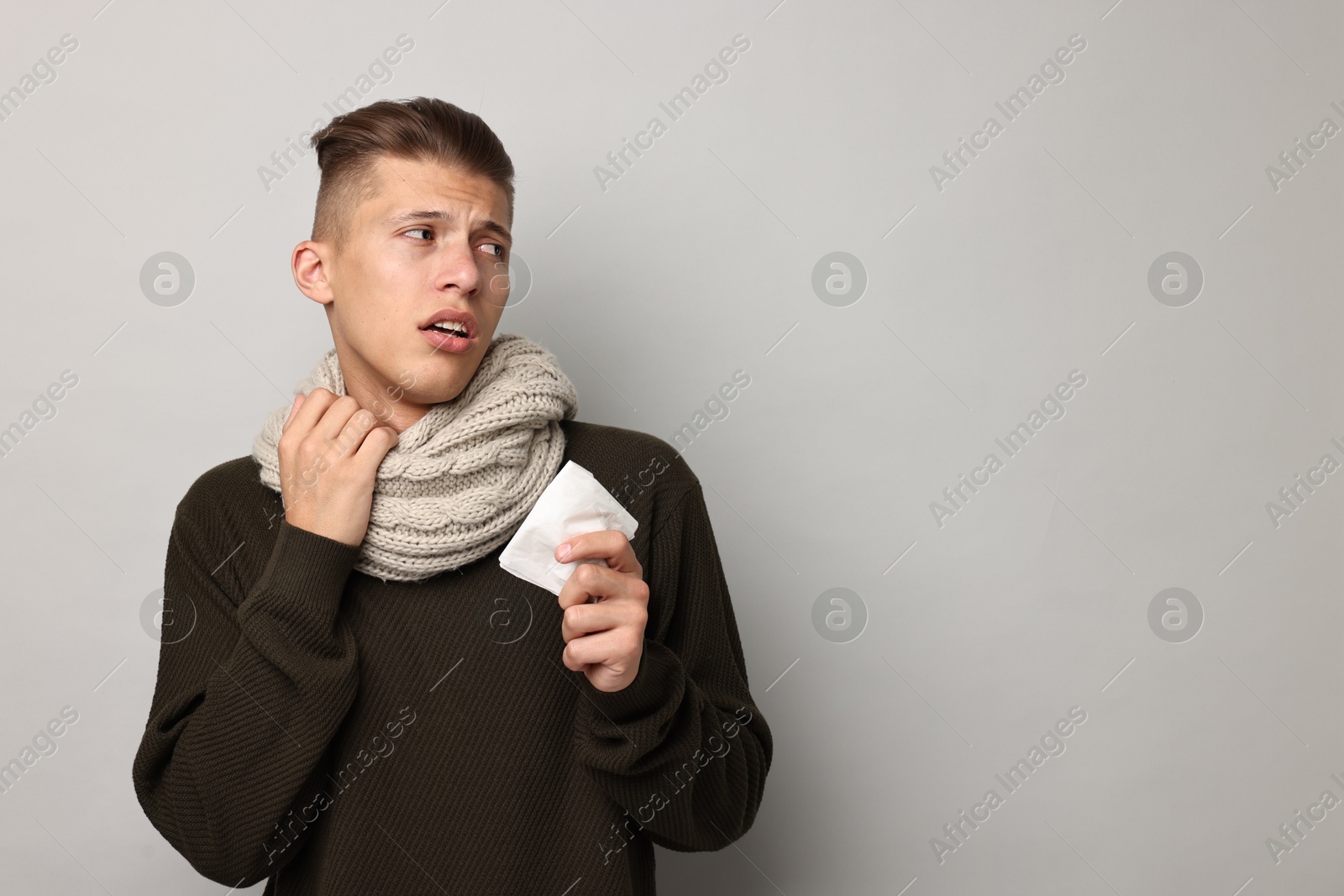 Photo of Sick man with tissue suffering from cold symptoms on light grey background, space for text