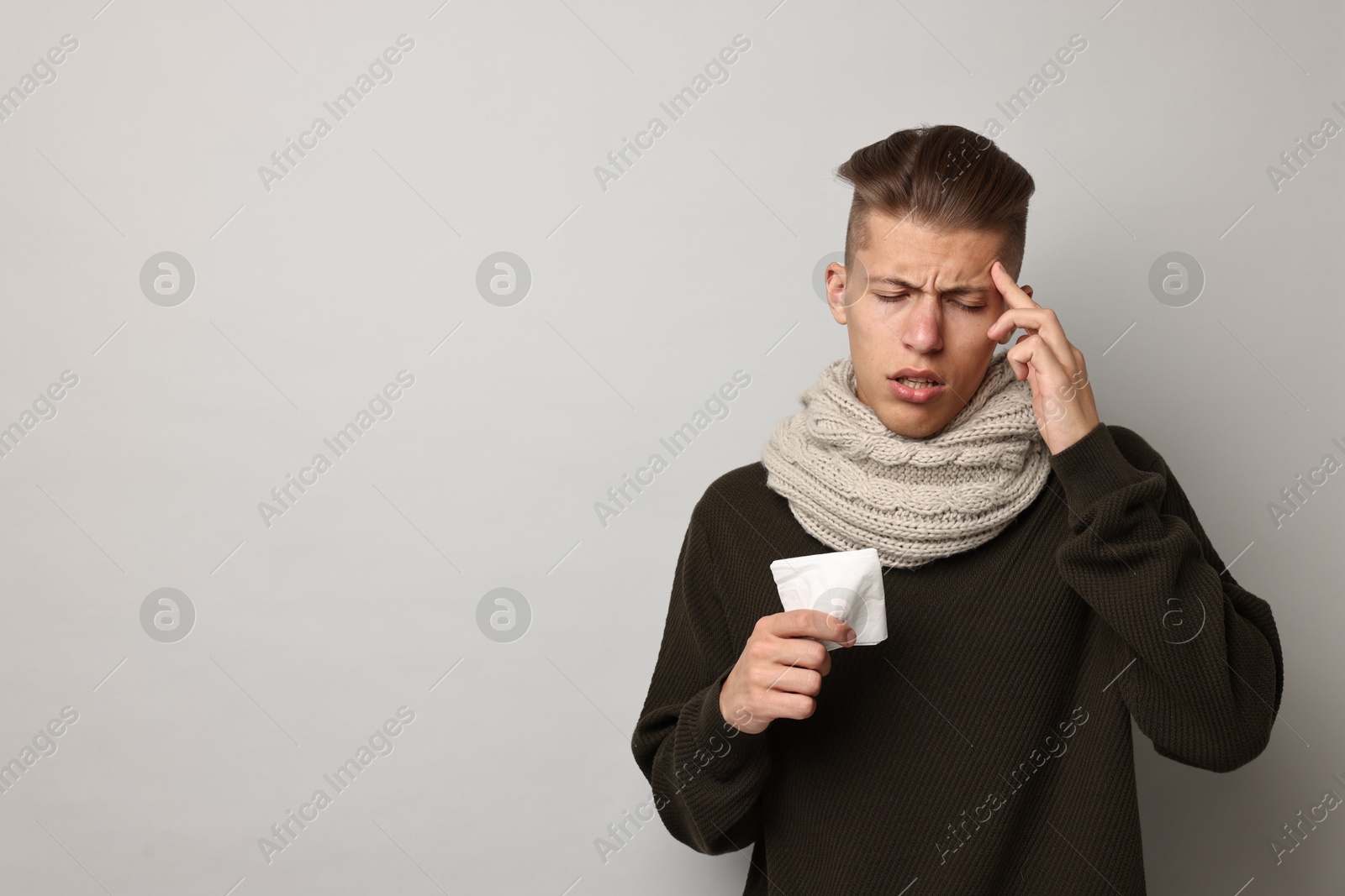 Photo of Sick man with tissue suffering from cold symptoms on light grey background, space for text