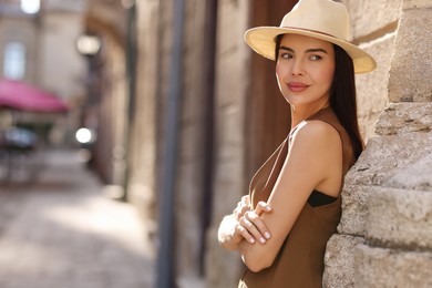 Photo of Beautiful young woman in stylish hat on city street, space for text