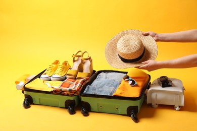 Woman packing suitcase for trip on yellow background, closeup