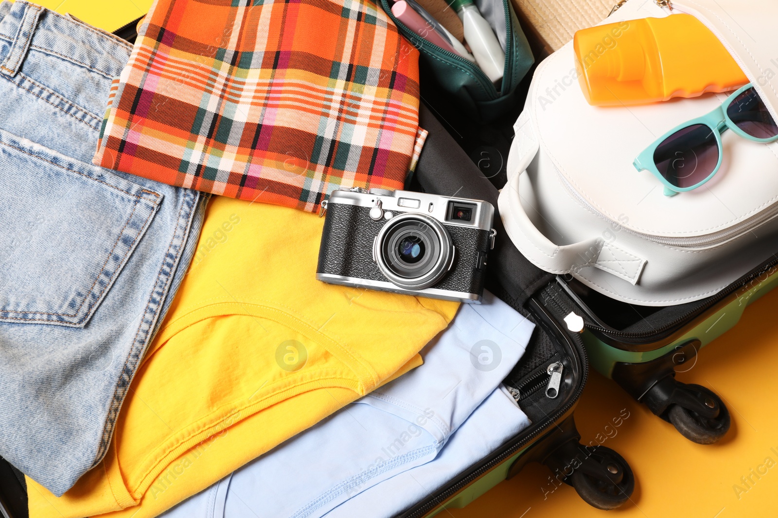 Photo of Open suitcase with traveler's belongings on yellow background, top view