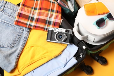 Open suitcase with traveler's belongings on yellow background, top view