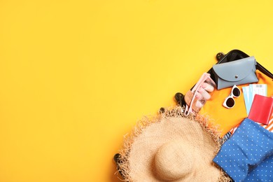 Open suitcase with traveler's belongings on yellow background, top view. Space for text