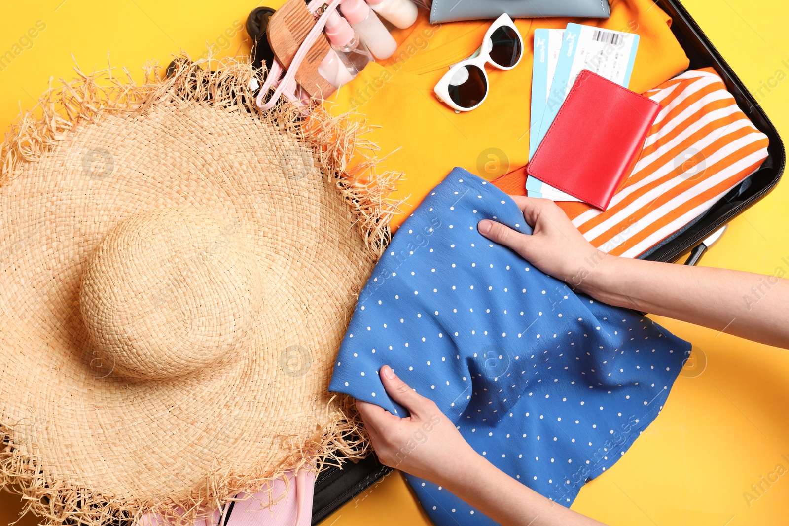 Photo of Woman packing suitcase for trip on yellow background, top view