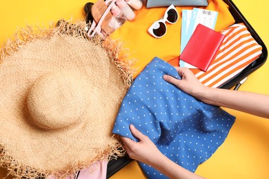 Photo of Woman packing suitcase for trip on yellow background, top view