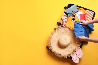 Photo of Woman packing suitcase on yellow background, top view. Space for text